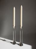 Two silver candle holders with white candles on a dark background
