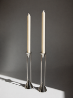 Two silver candle holders with white candles on a dark background