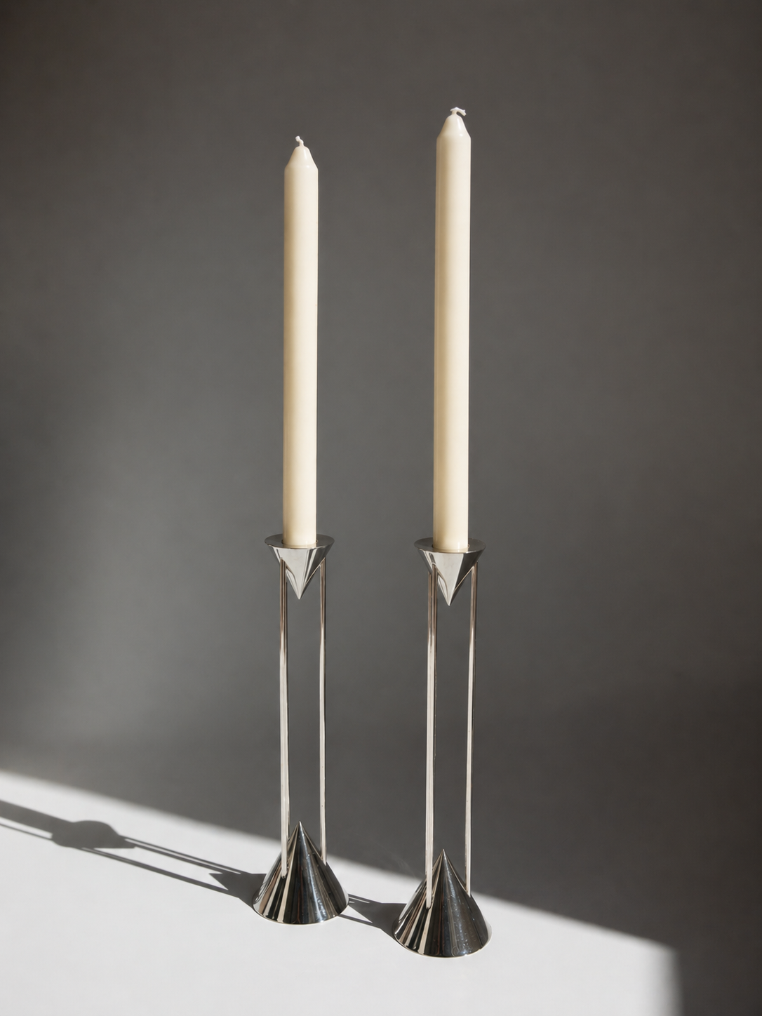 Two silver candle holders with white candles on a dark background